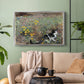 Silver floater framed canvas featuring a naturalistic depiction of cat in blooming countryside setting, displayed above a sofa in a modern living room.