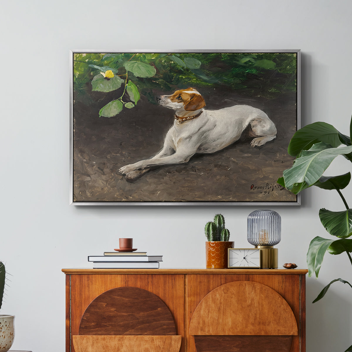 Portrait of a Dog, 1891 by Bruno Liljefors in a silver floater framed canvas featuring a dog lying on ground with head raised in natural outdoor setting, displayed above a wood console cabinet.