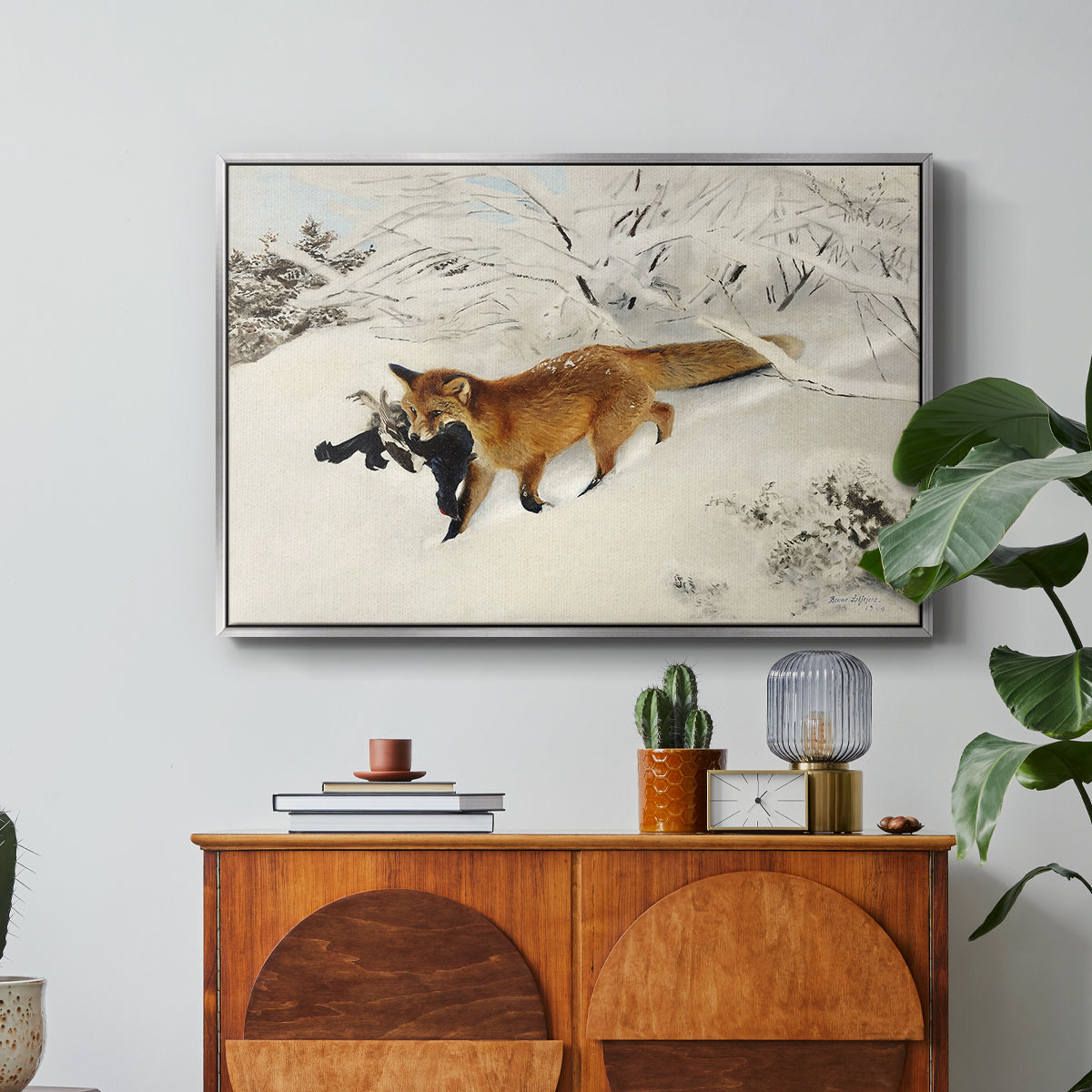 Fox in Snow Landscape, 1900 by Bruno Liljefors in a silver floater framed canvas featuring a fox running across snowy landscape with sparse vegetation, displayed above a wood console cabinet.