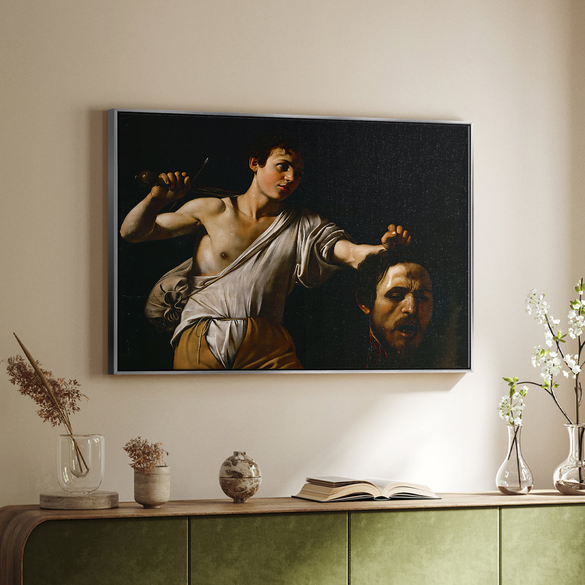 Silver floater framed canvas of David with the Head of Goliath (Vienna Version), c. 1607 by Caravaggio, featuring a biblical scene of David gripping Goliath's head with dramatic lighting above a sideboard in a softly lit hallway.