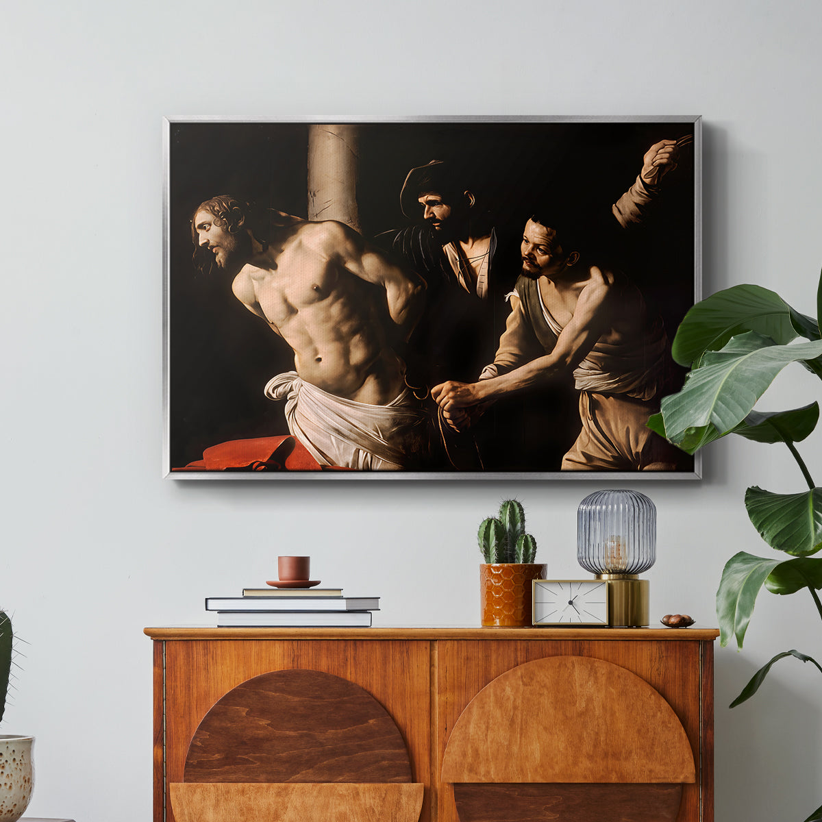 The Flagellation of Christ at the Column (Rouen Version), 1606 by Caravaggio in a silver floater framed canvas featuring Christ bound to column while being whipped by surrounding figures, displayed above a wood console cabinet.