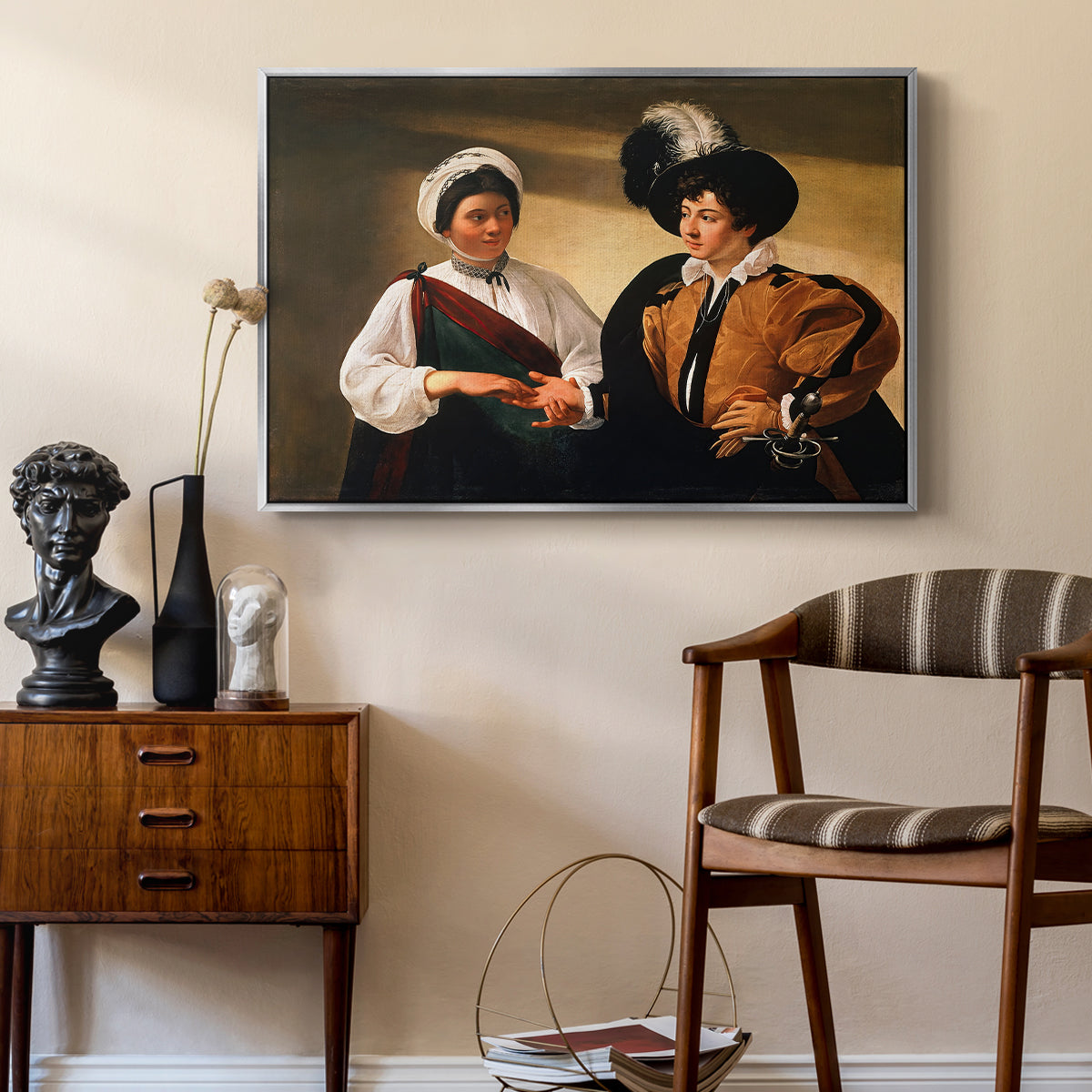 The Fortune Teller (Louvre Version), c. 1595 by Caravaggio as a silver floater framed canvas featuring an intimate scene of palm reading with subtle act of theft, styled above a mid-century console in a contemporary living area.