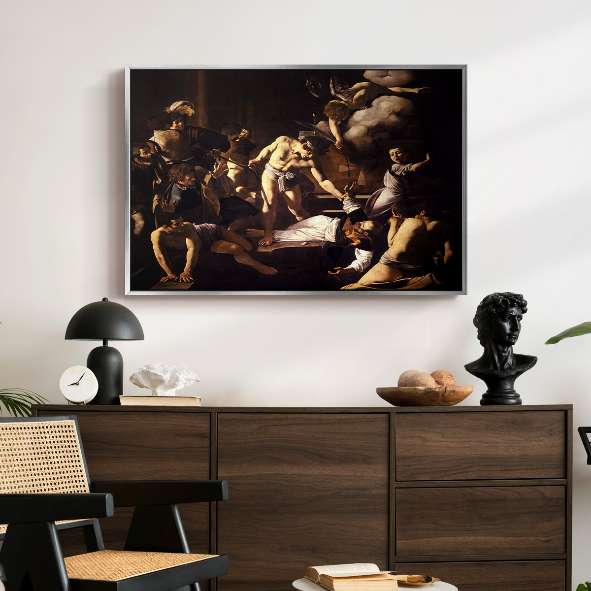 The Martyrdom of Saint Matthew, 1599-1600 by Caravaggio displayed in a silver floater framed canvas above a dark wood credenza in an entryway.
