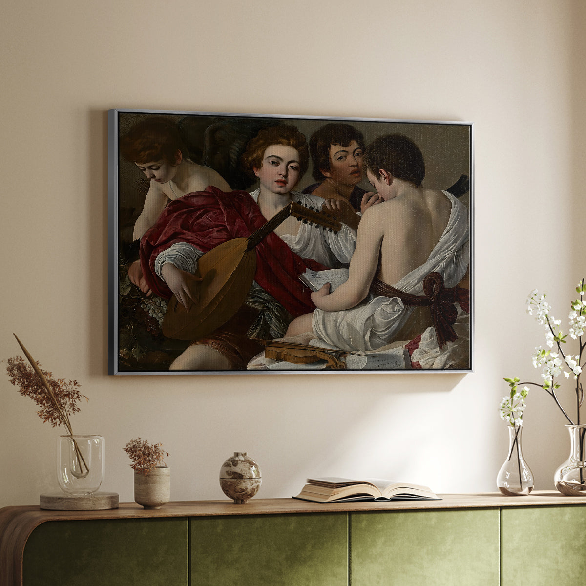 Silver floater framed canvas of The Musicians, c. 1595 by Caravaggio, featuring an ensemble of musicians holding lute and singing in close arrangement above a sideboard in a softly lit hallway.
