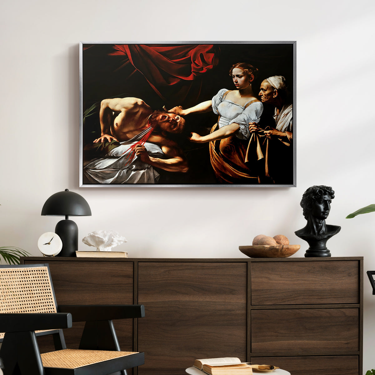 Judith Beheading Holofernes, c. 1599 by Caravaggio displayed in a silver floater framed canvas above a dark wood credenza in an entryway.