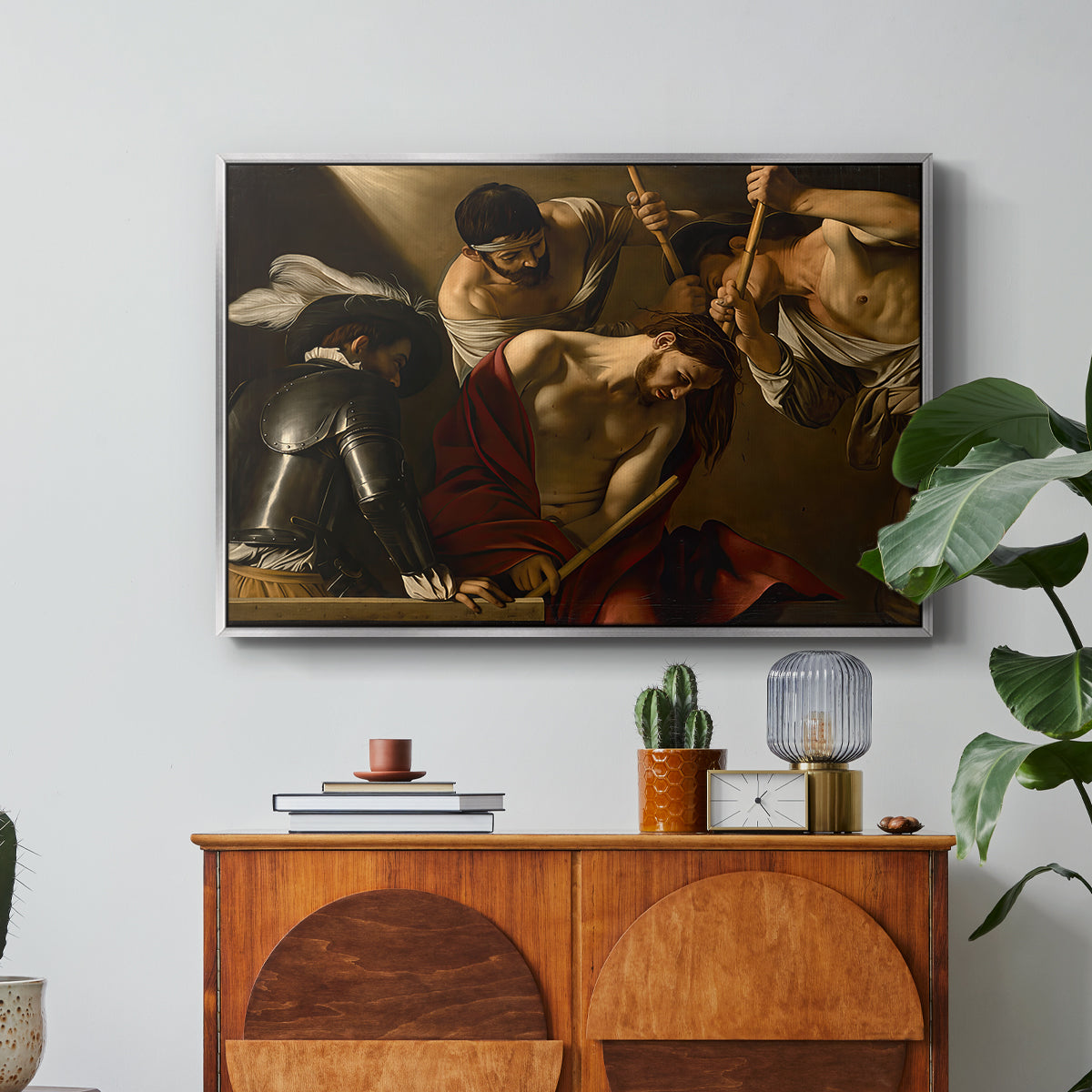 The Crowning with Thorns (Vienna Version), c. 1602-1604 by Caravaggio in a silver floater framed canvas featuring Christ surrounded by men pressing crown of thorns onto his head, displayed above a wood console cabinet.