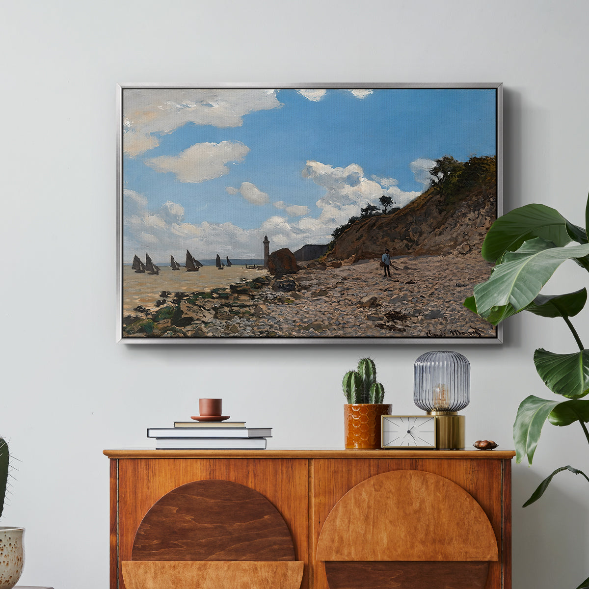 The Beach at Honfleur, 1864 by Claude Monet in a silver floater framed canvas featuring a coastal beach scene with figures gathered along shoreline and boats nearby, displayed above a wood console cabinet.