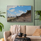 Silver floater framed canvas featuring a coastal landscape with boats and people along shore, displayed above a sofa in a modern living room.