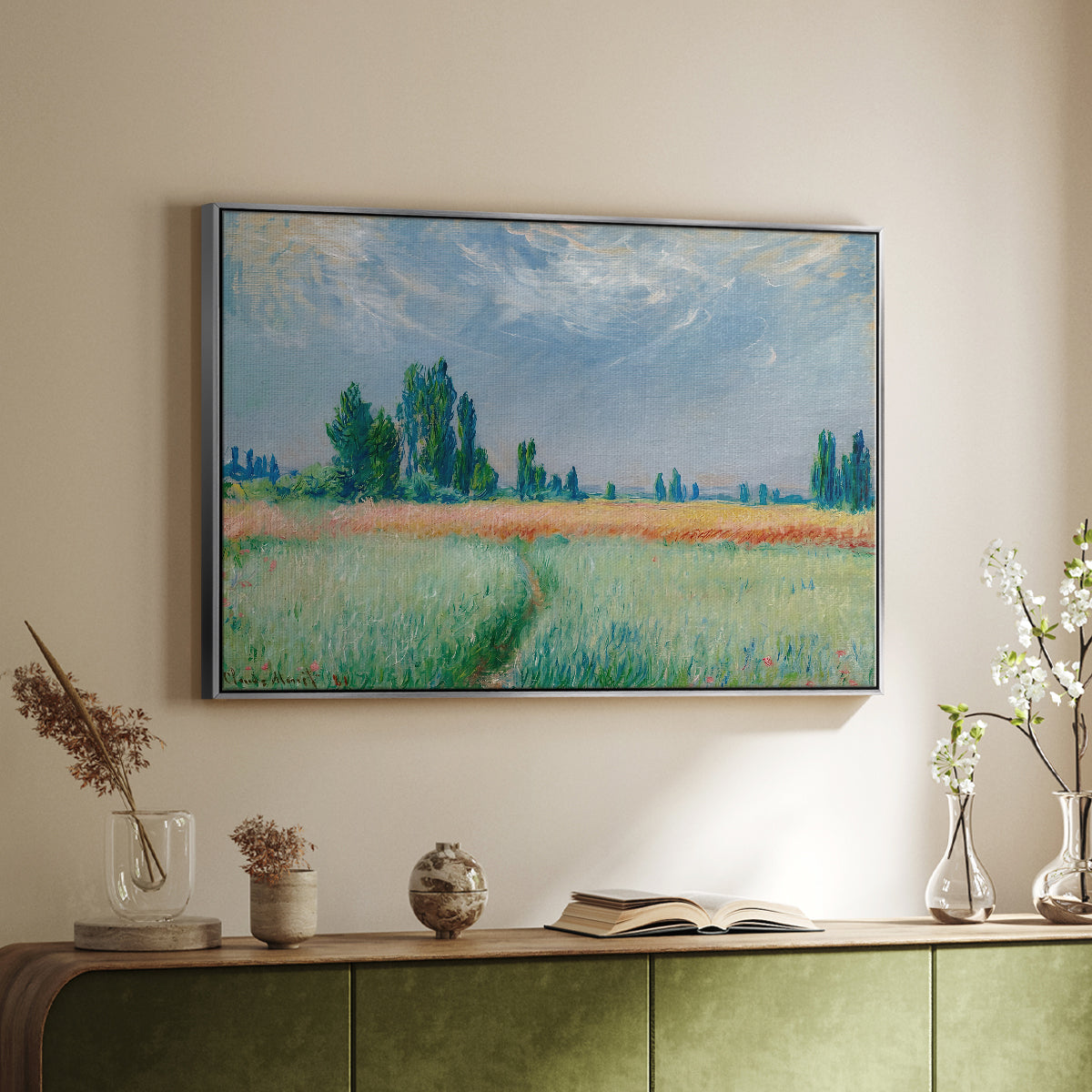 Silver floater framed canvas of The Wheat Field (Champ de Blé), 1881 by Claude Monet, featuring an impressionist depiction of ripened grain field in countryside above a sideboard in a softly lit hallway.