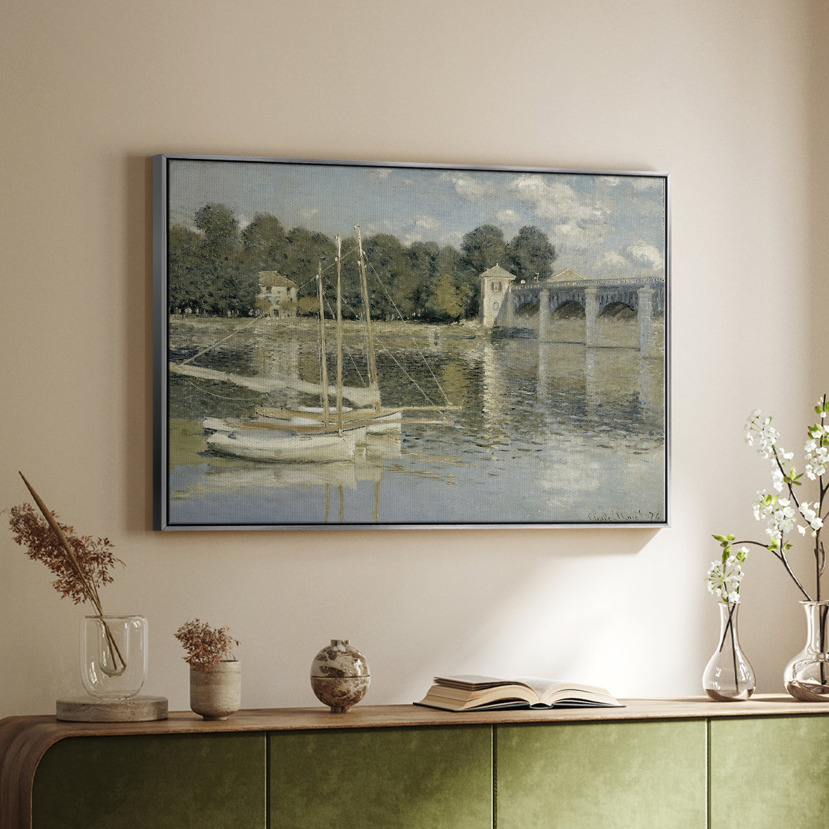 Silver floater framed canvas of The Bridge at Argenteuil, 1874 by Claude Monet, featuring an impressionist river scene with boats passing beneath bridge above a sideboard in a softly lit hallway.