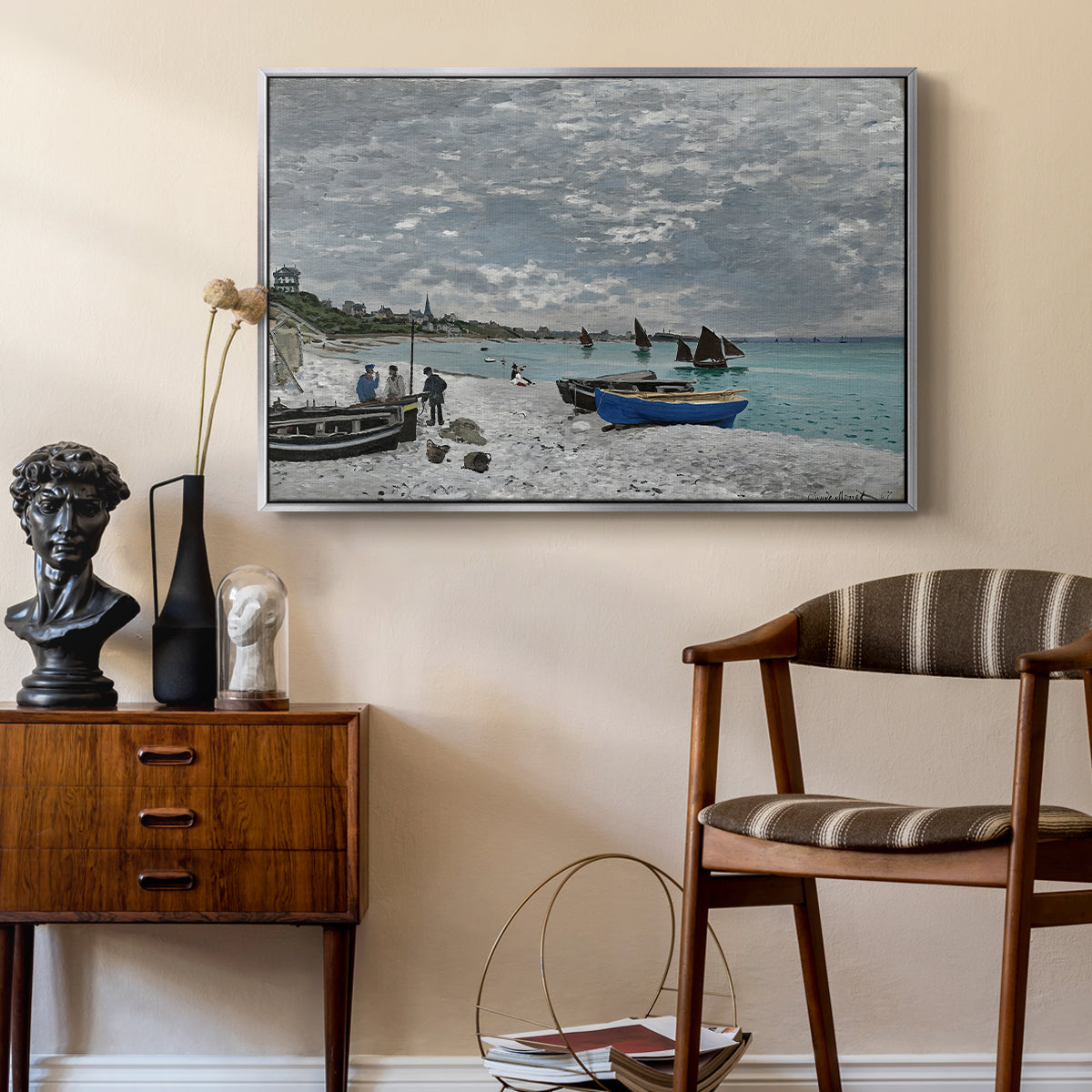 The Beach at Sainte-Adresse, 1867 by Claude Monet as a silver floater framed canvas featuring a coastal landscape with sailboats and visitors on cliffside, styled above a mid-century console in a contemporary living area.