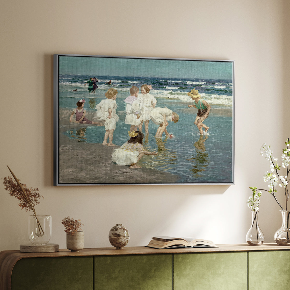 Silver floater framed canvas of A Holiday, c. 1915 by Edward Henry Potthast, featuring a beach scene with figures bathing and standing in waves under bright sky above a sideboard in a softly lit hallway.