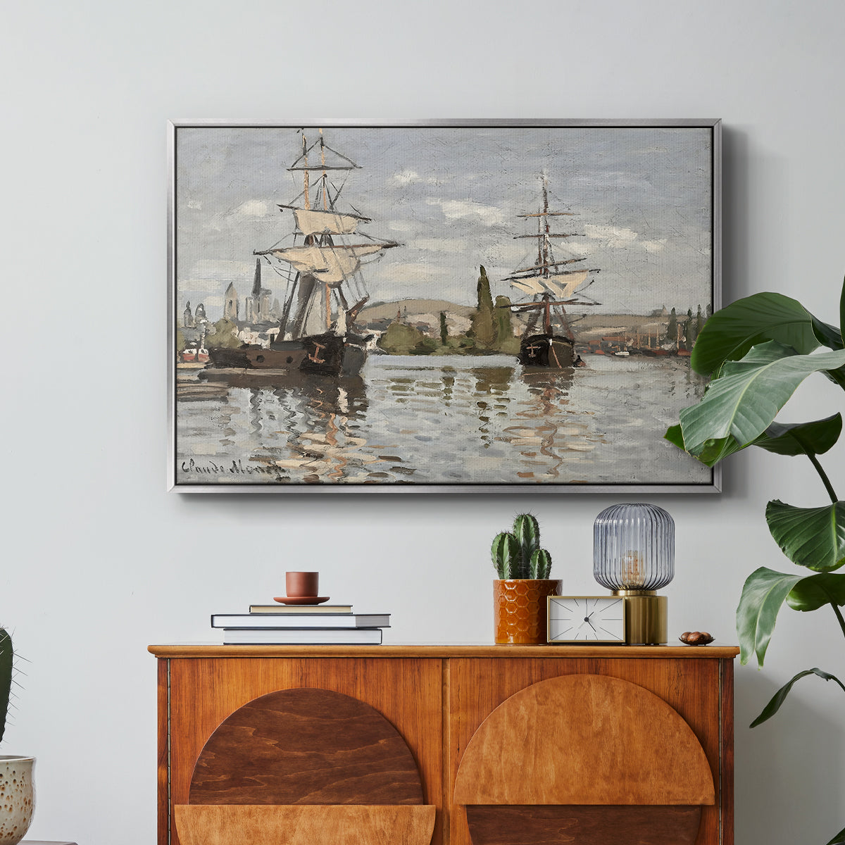 Ships Riding on the Seine at Rouen, 1872 by Claude Monet in a silver floater framed canvas featuring large ships docked along the Seine with masts rising against soft sky, displayed above a wood console cabinet.