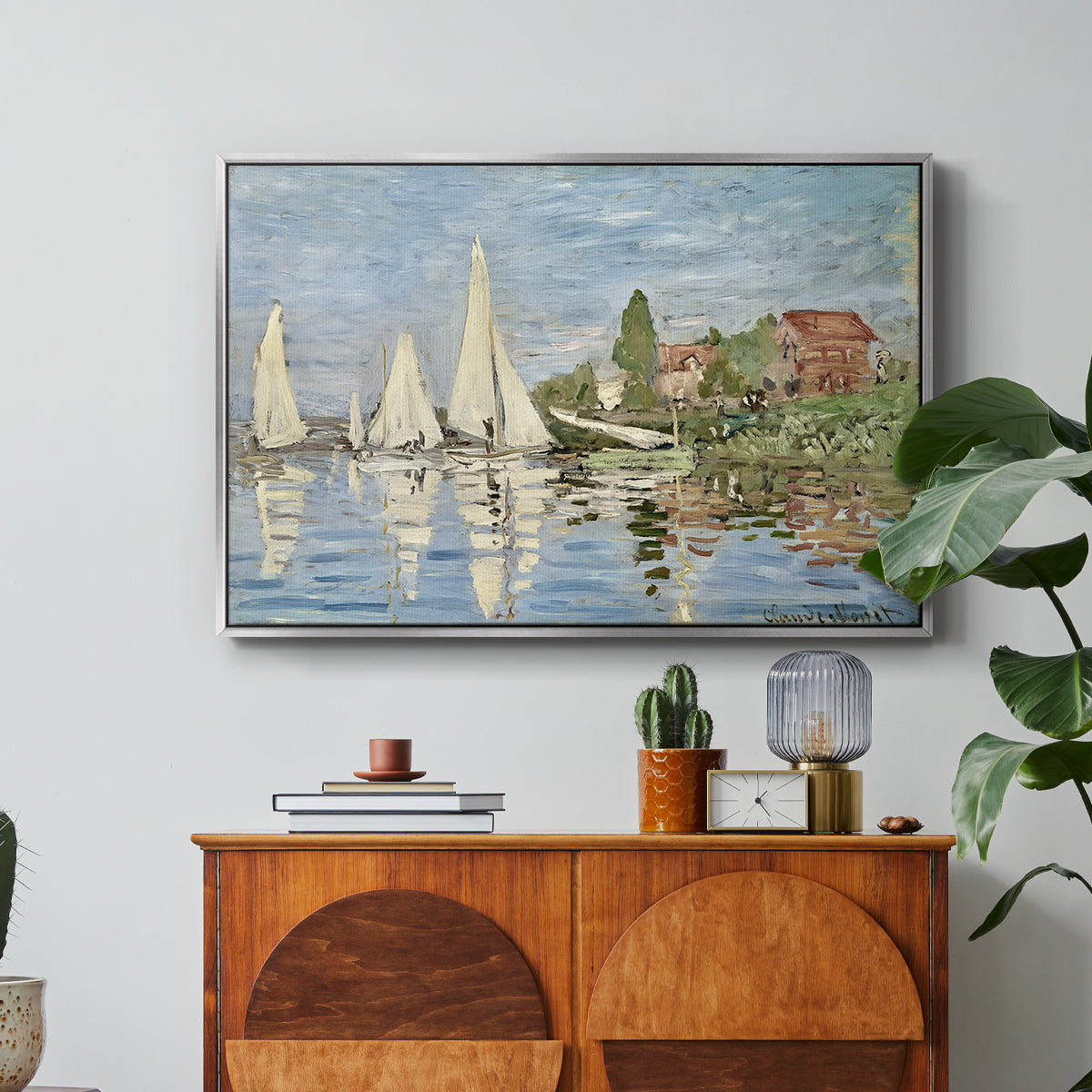 Regatta at Argenteuil, 1872 by Claude Monet in a silver floater framed canvas featuring colorful sailboats racing across river under bright sky, displayed above a wood console cabinet.