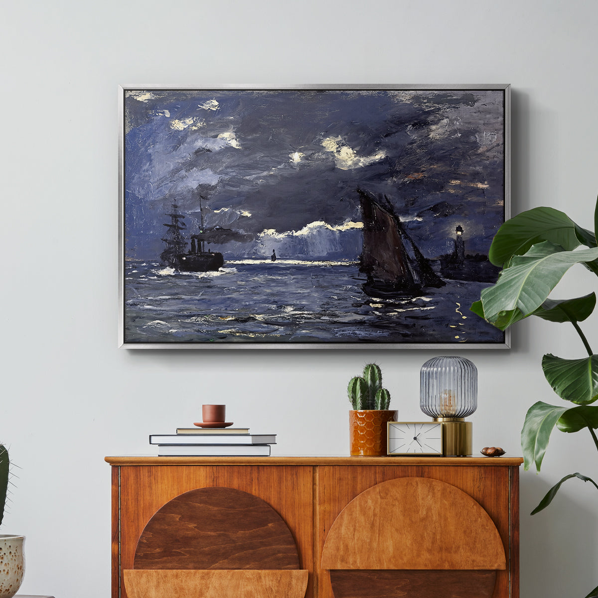 A Seascape, Shipping by Moonlight, 1864 by Claude Monet in a silver floater framed canvas featuring ships on dark sea illuminated by moonlight under night sky, displayed above a wood console cabinet.