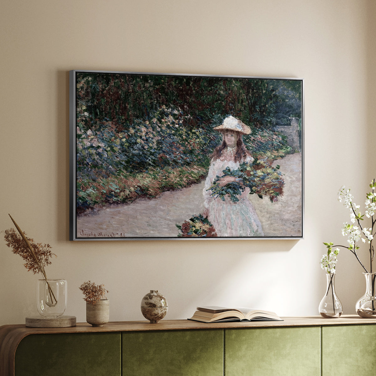 Silver floater framed canvas of Young Girl in the Garden at Giverny, 1888 by Claude Monet, featuring an impressionist garden scene with child among greenery and blossoms above a sideboard in a softly lit hallway.