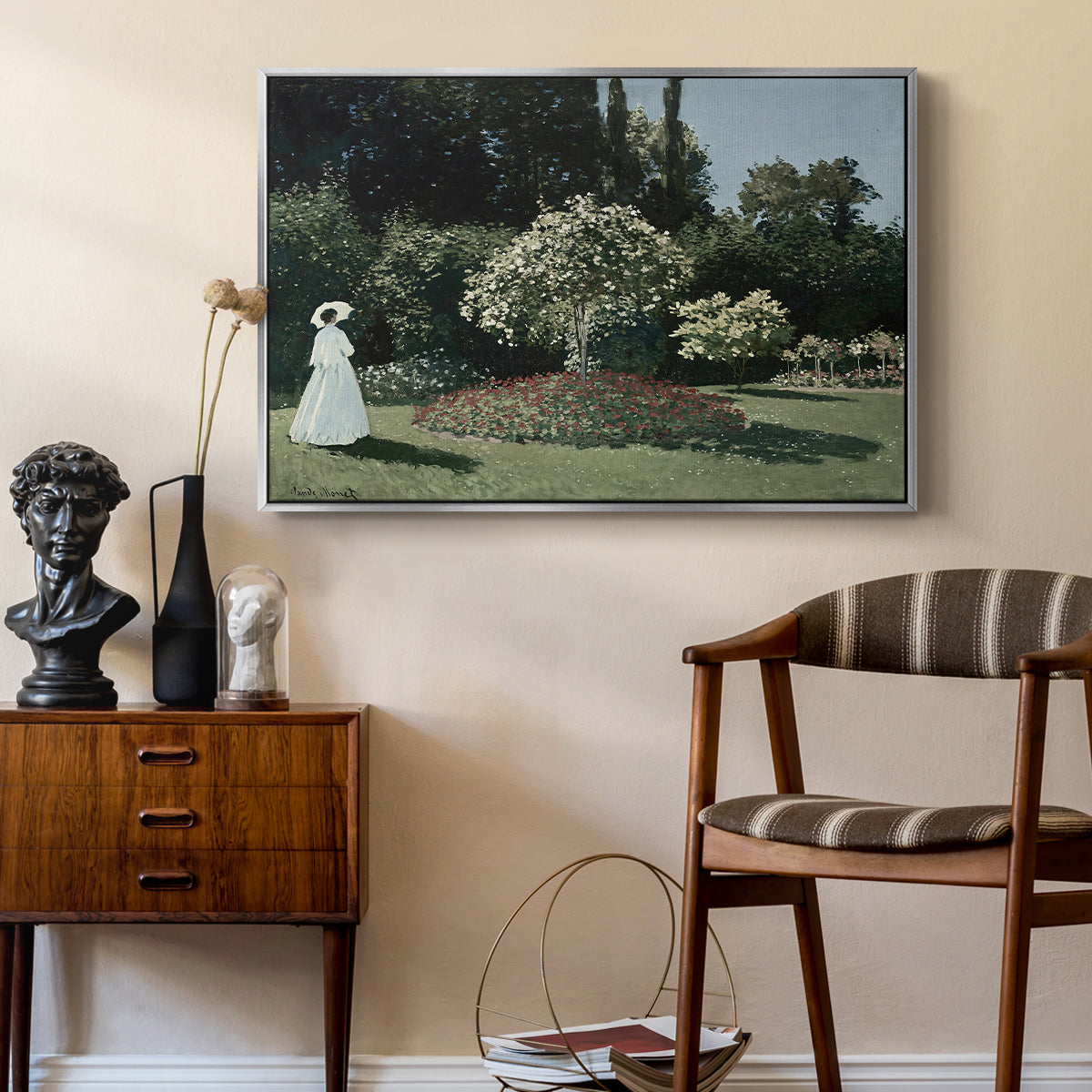 Woman in the Garden, Sainte-Adresse, 1867 by Claude Monet as a silver floater framed canvas featuring an elegant woman posed outdoors among blooming plants, styled above a mid-century console in a contemporary living area.