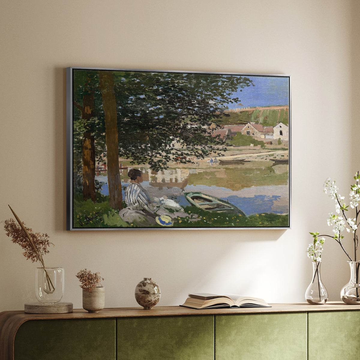 Silver floater framed canvas of On the Bank of the Seine, Bennecourt, 1868 by Claude Monet, featuring a peaceful riverside scene with figures resting in grassy area by water above a sideboard in a softly lit hallway.