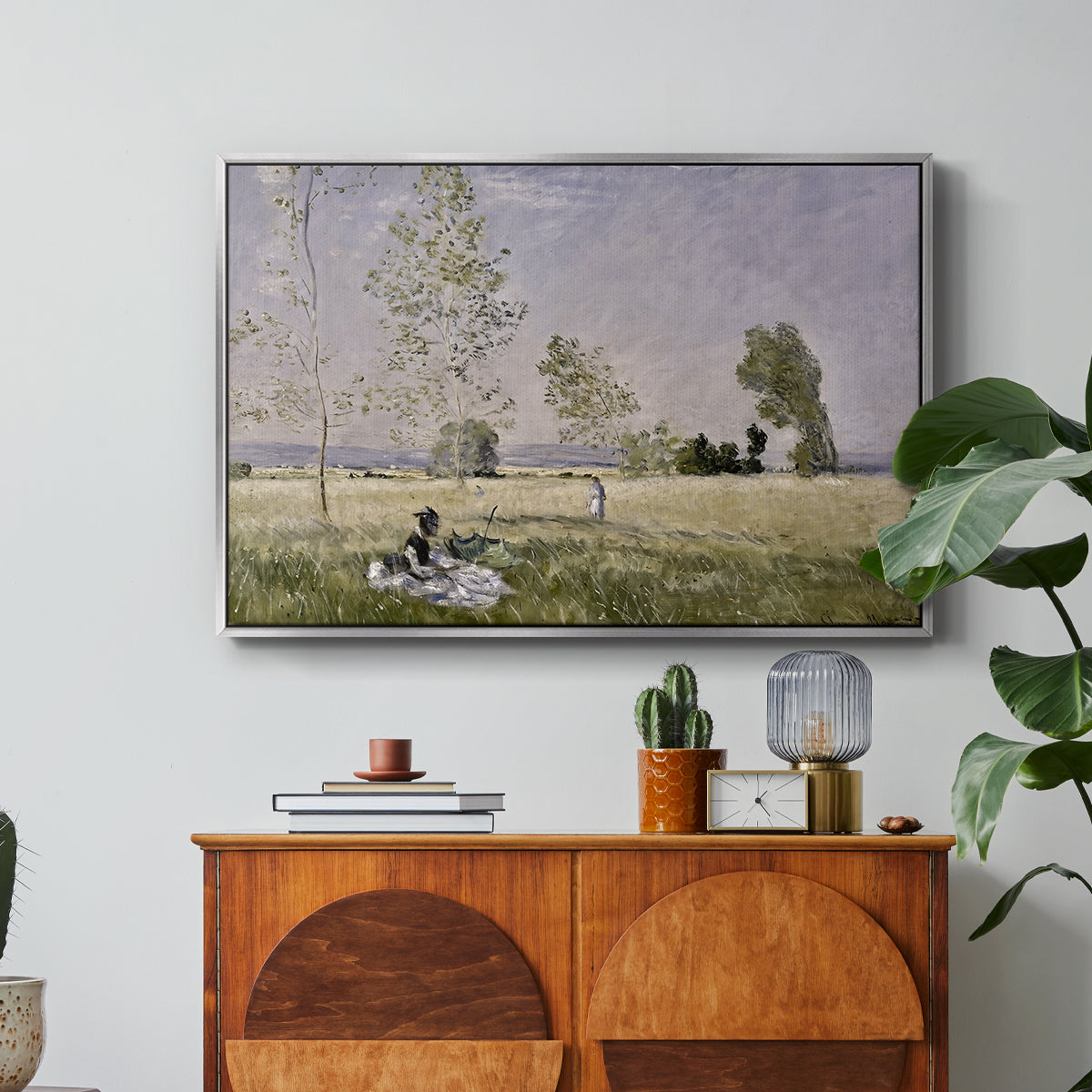 Summer (L'ete), 1874 by Claude Monet in a silver floater framed canvas featuring a woman seated in grassy field beneath tree in bright summer landscape, displayed above a wood console cabinet.