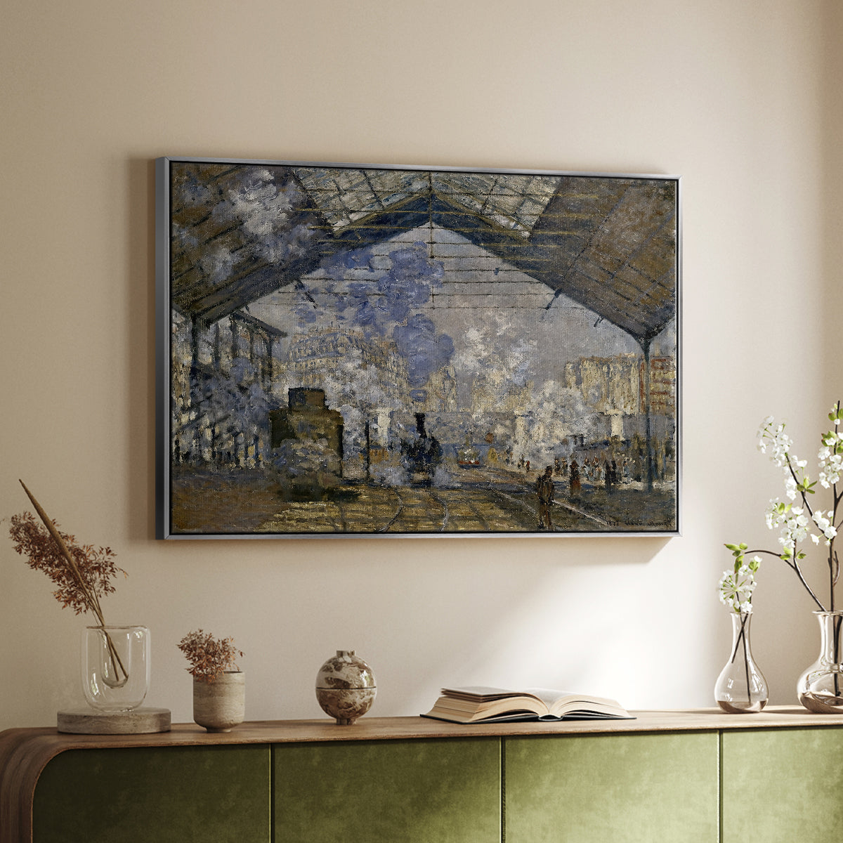 Silver floater framed canvas of The Gare Saint-Lazare, 1877 by Claude Monet, featuring an impressionist scene of trains and smoke inside busy railway station above a sideboard in a softly lit hallway.