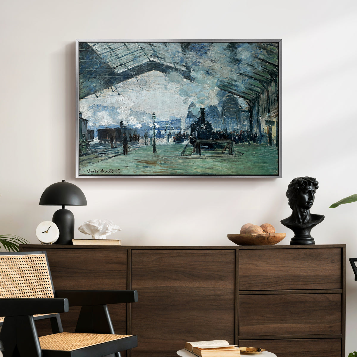The Saint-Lazare Station, 1877 by Claude Monet displayed in a silver floater framed canvas above a dark wood credenza in an entryway.