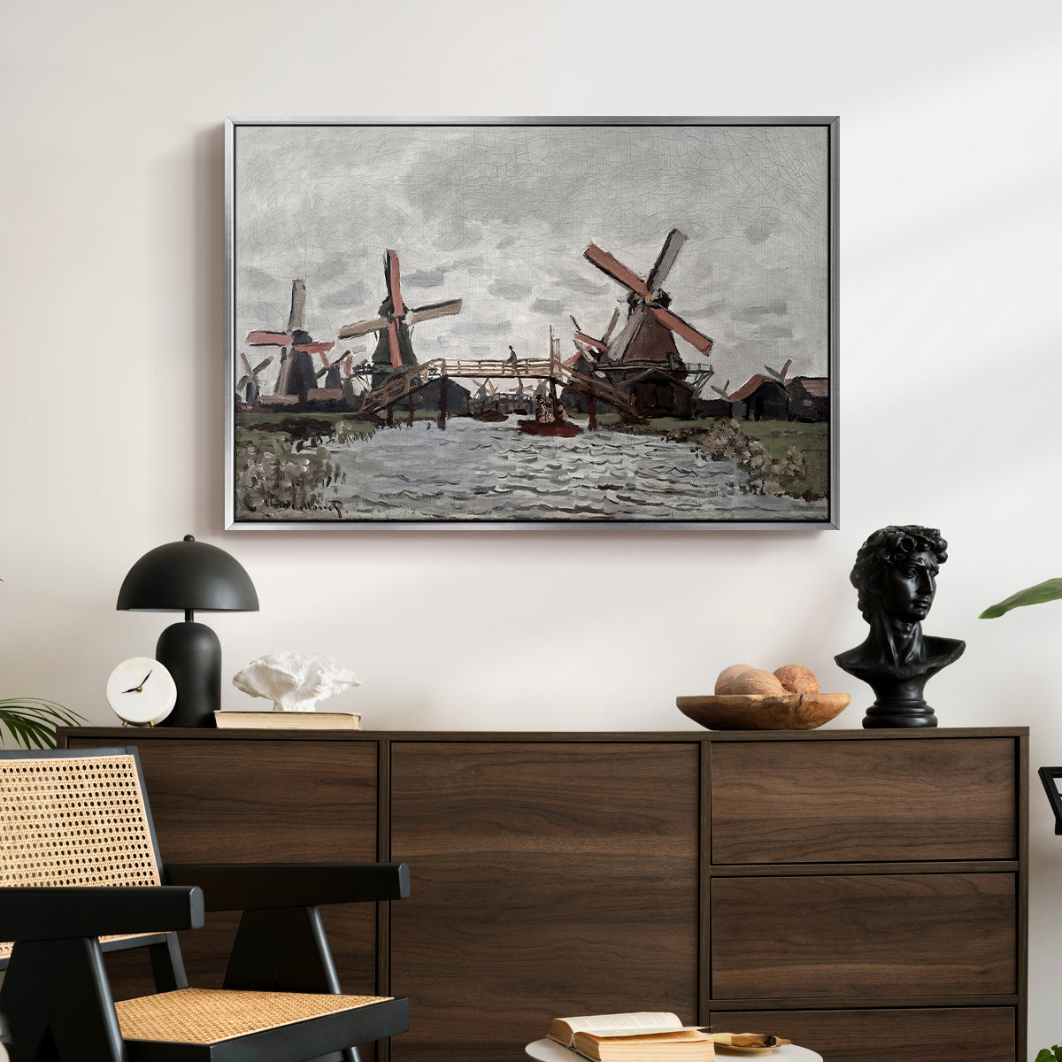 Windmills near Zaandam, 1871 by Claude Monet displayed in a silver floater framed canvas above a dark wood credenza in an entryway.