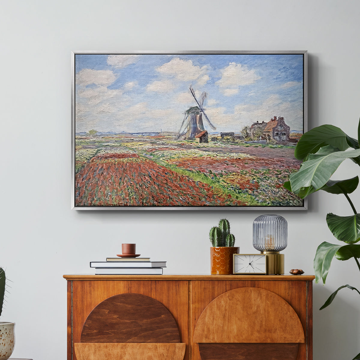 Tulip Fields with the Rijnsburg Windmill, 1886 by Claude Monet in a silver floater framed canvas featuring colorful rows of tulip fields leading toward distant windmill, displayed above a wood console cabinet.