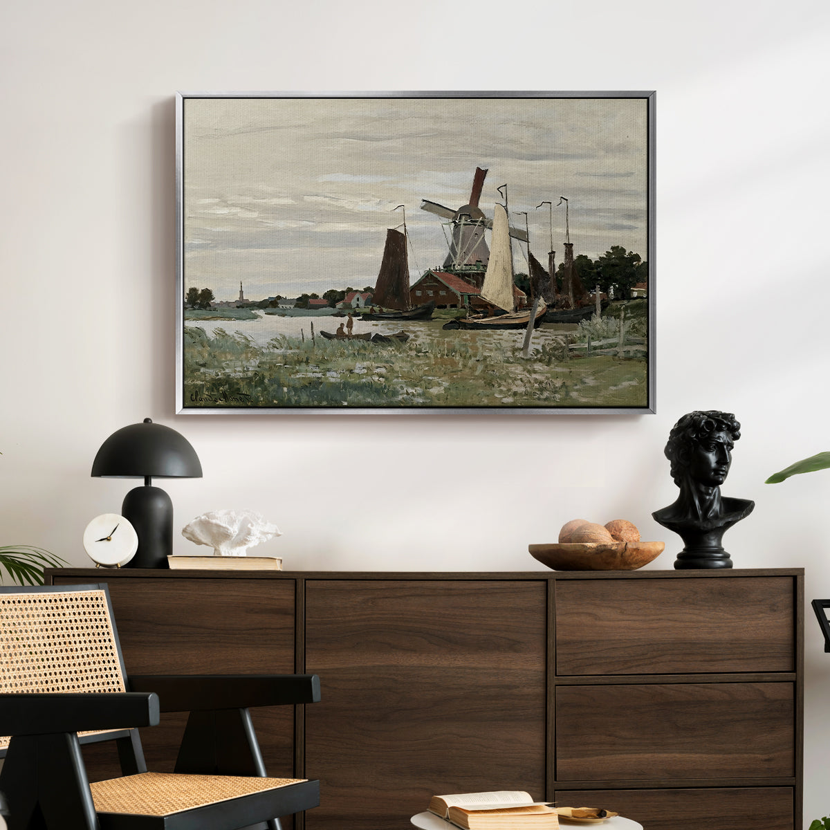 Windmill at Zaandam, 1871 by Claude Monet displayed in a silver floater framed canvas above a dark wood credenza in an entryway.