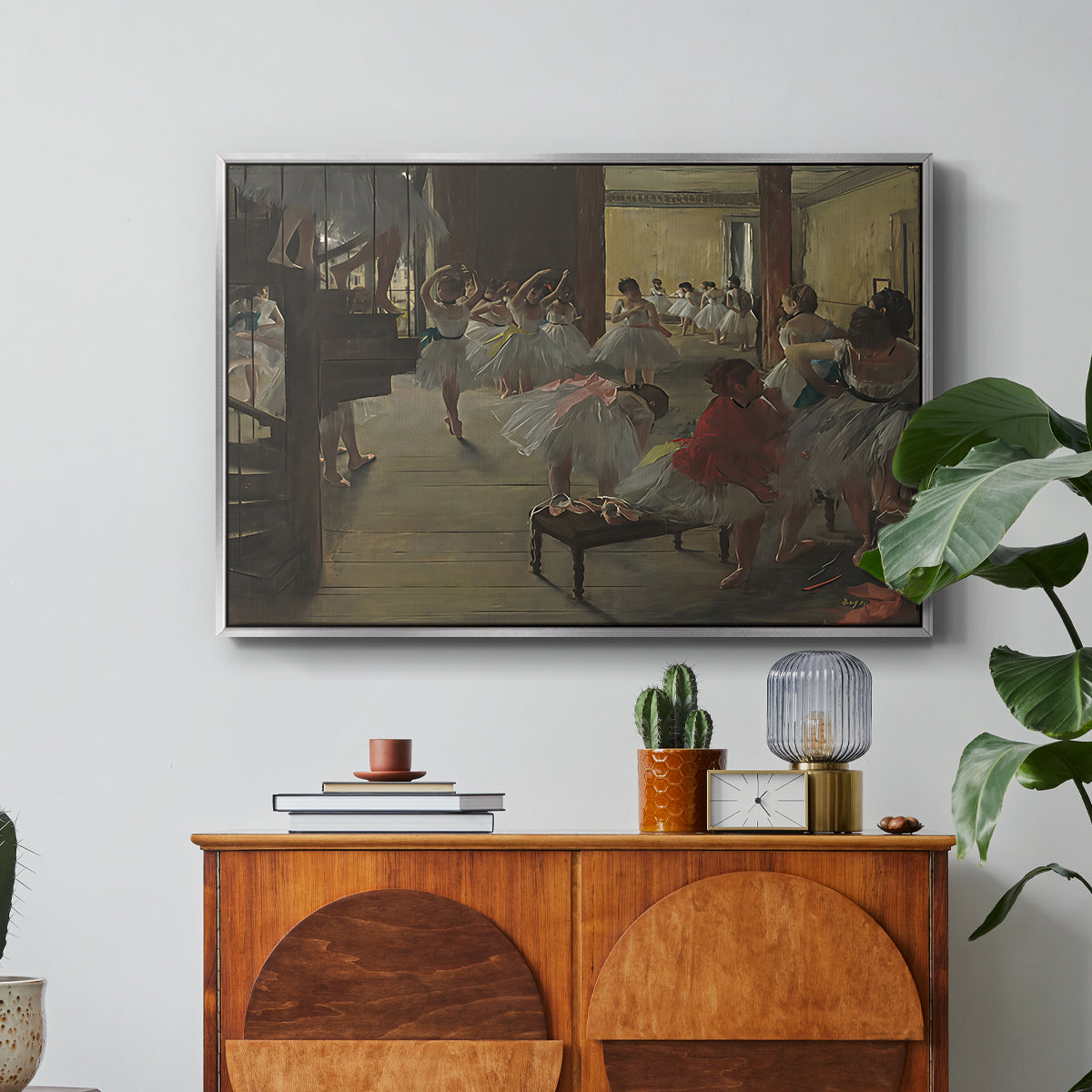 The Dance Class, c. 1873 by Edgar Degas in a silver floater framed canvas featuring ballerinas practicing in studio with instructor observing nearby, displayed above a wood console cabinet.