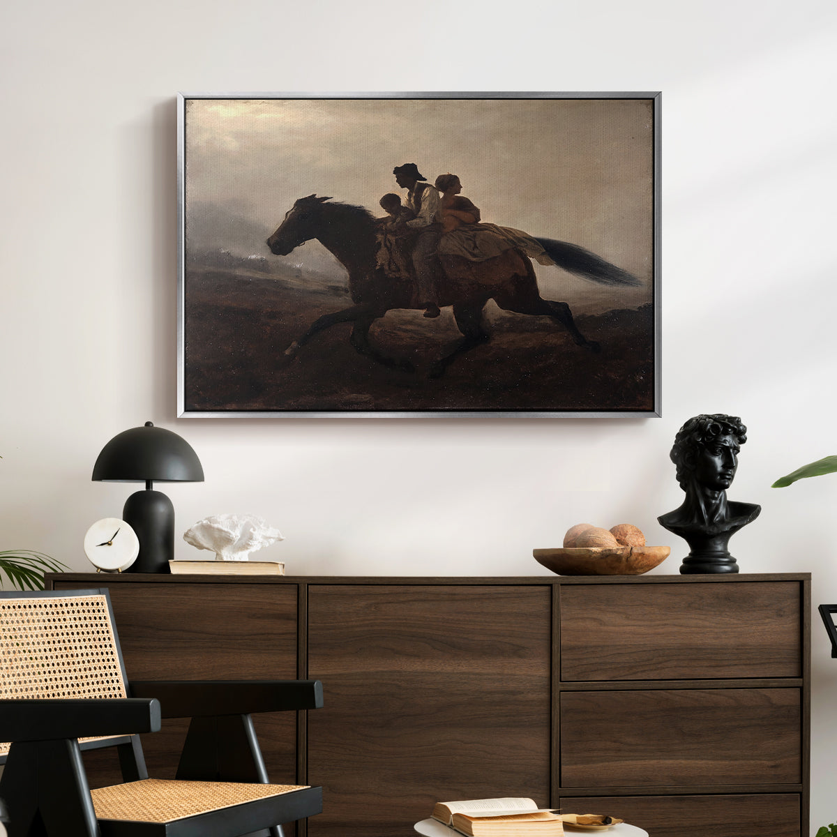 A Ride for Liberty – The Fugitive Slaves, c. 1862 by Eastman Johnson displayed in a silver floater framed canvas above a dark wood credenza in an entryway.