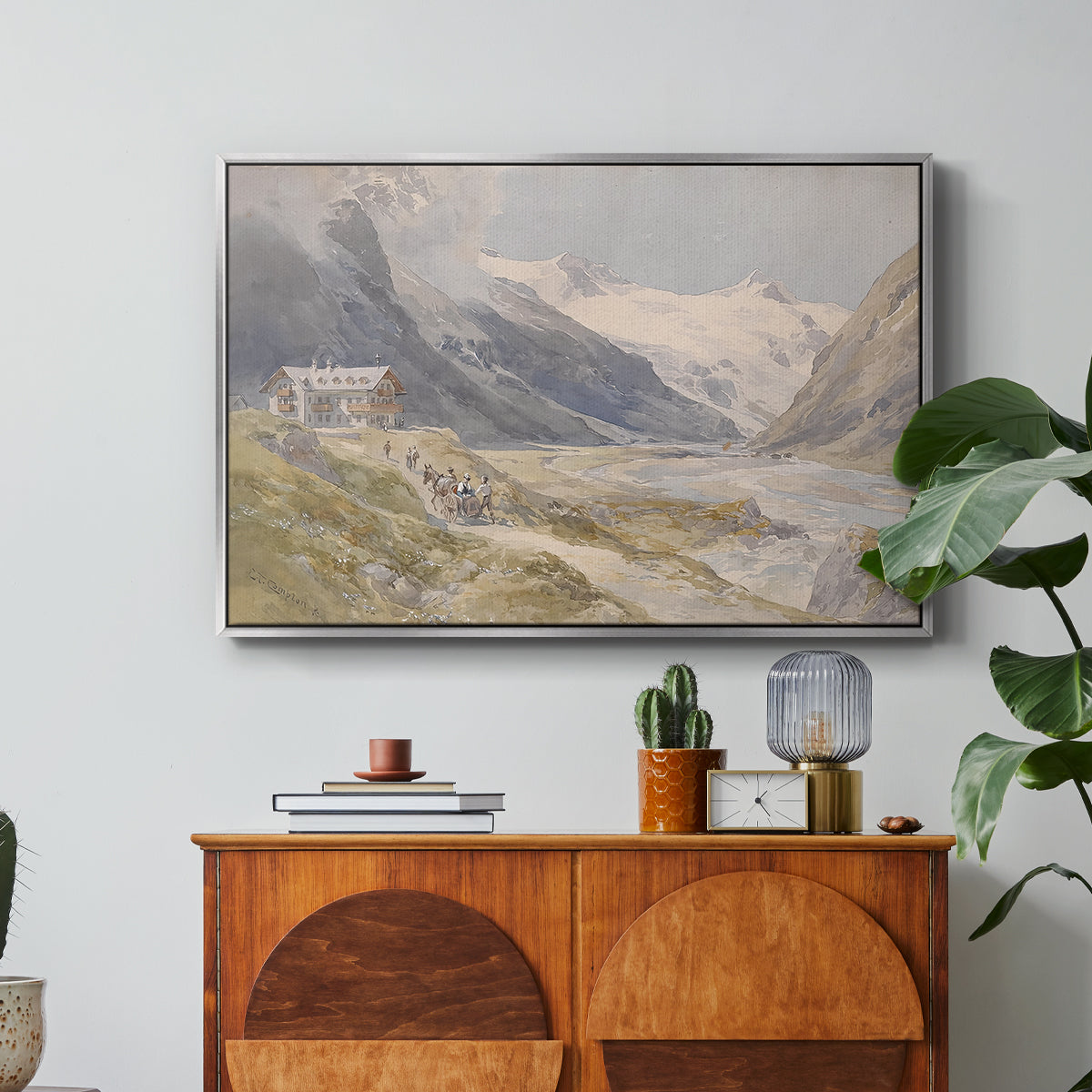 Shepherds (Pasterze), c. 1921 by Edward Theodore Compton in a silver floater framed canvas featuring a small group of shepherds in alpine landscape with grazing animals, displayed above a wood console cabinet.