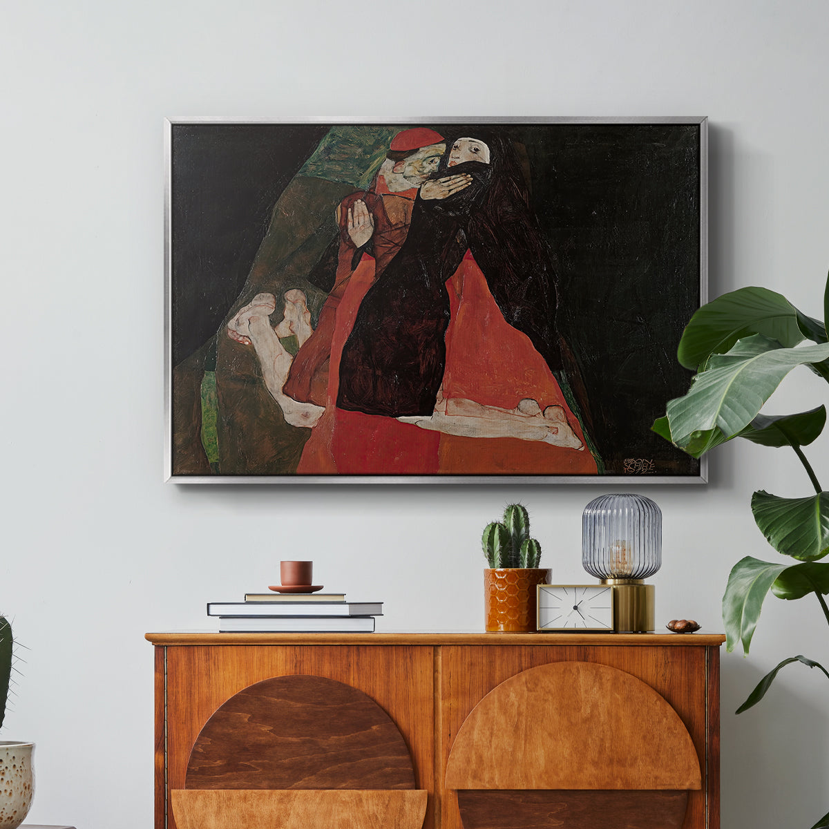 Cardinal and Nun (Caress), 1912 by Egon Schiele in a silver floater framed canvas featuring two figures embracing intimately in stylized expressionist composition, displayed above a wood console cabinet.