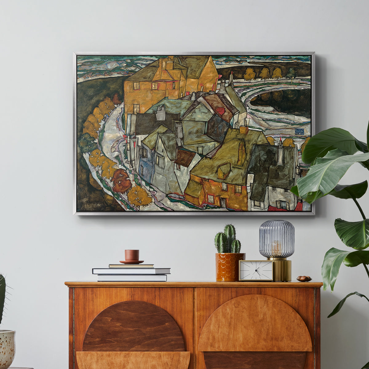 Crescent of Houses II (Island Town), 1915 by Egon Schiele in a silver floater framed canvas featuring a curved row of colorful houses forming crescent shape along water, displayed above a wood console cabinet.