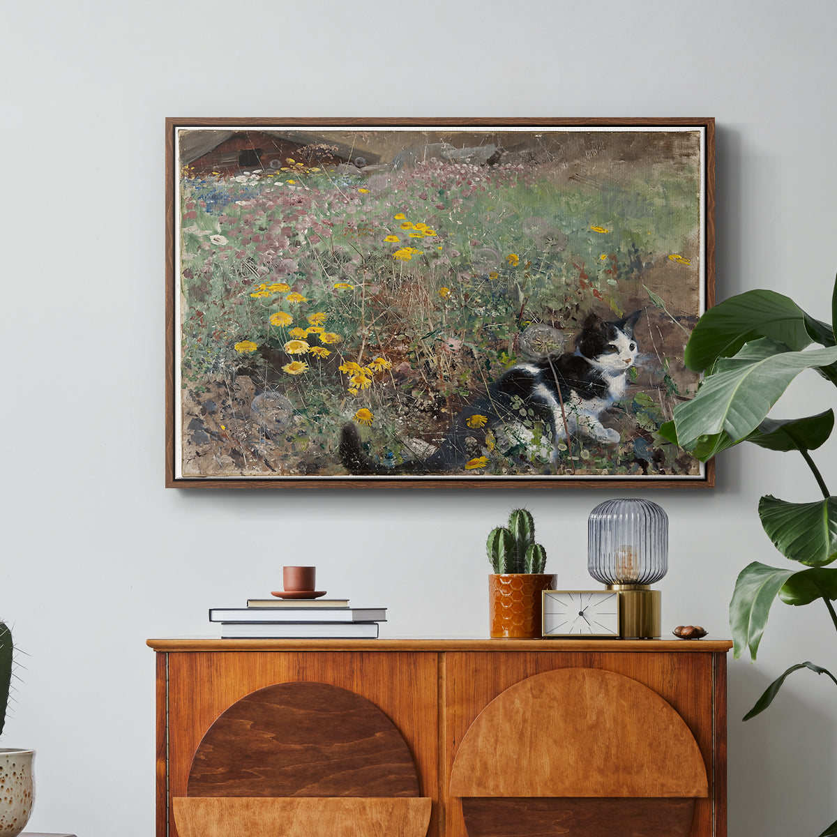 Cat on a Flowery Meadow, 1887 by Bruno Liljefors in a walnut floater framed canvas featuring a cat crouching in a meadow filled with wildflowers and greenery, displayed above a wood console cabinet.