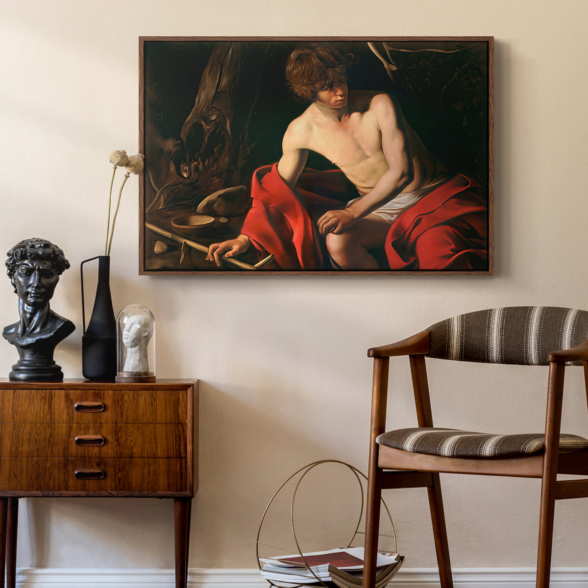 Saint John the Baptist in the Wilderness, c. 1603-1604 by Caravaggio as a walnut floater framed canvas featuring a biblical youth seated outdoors with symbolic staff and minimal landscape, styled above a mid-century console in a contemporary living area.