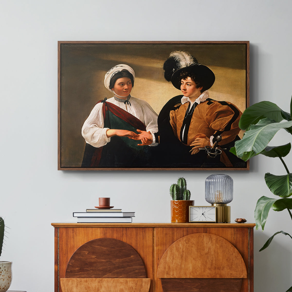 The Fortune Teller (Louvre Version), c. 1595 by Caravaggio in a walnut floater framed canvas featuring a woman reading a young man's palm while secretly stealing his ring, displayed above a wood console cabinet.