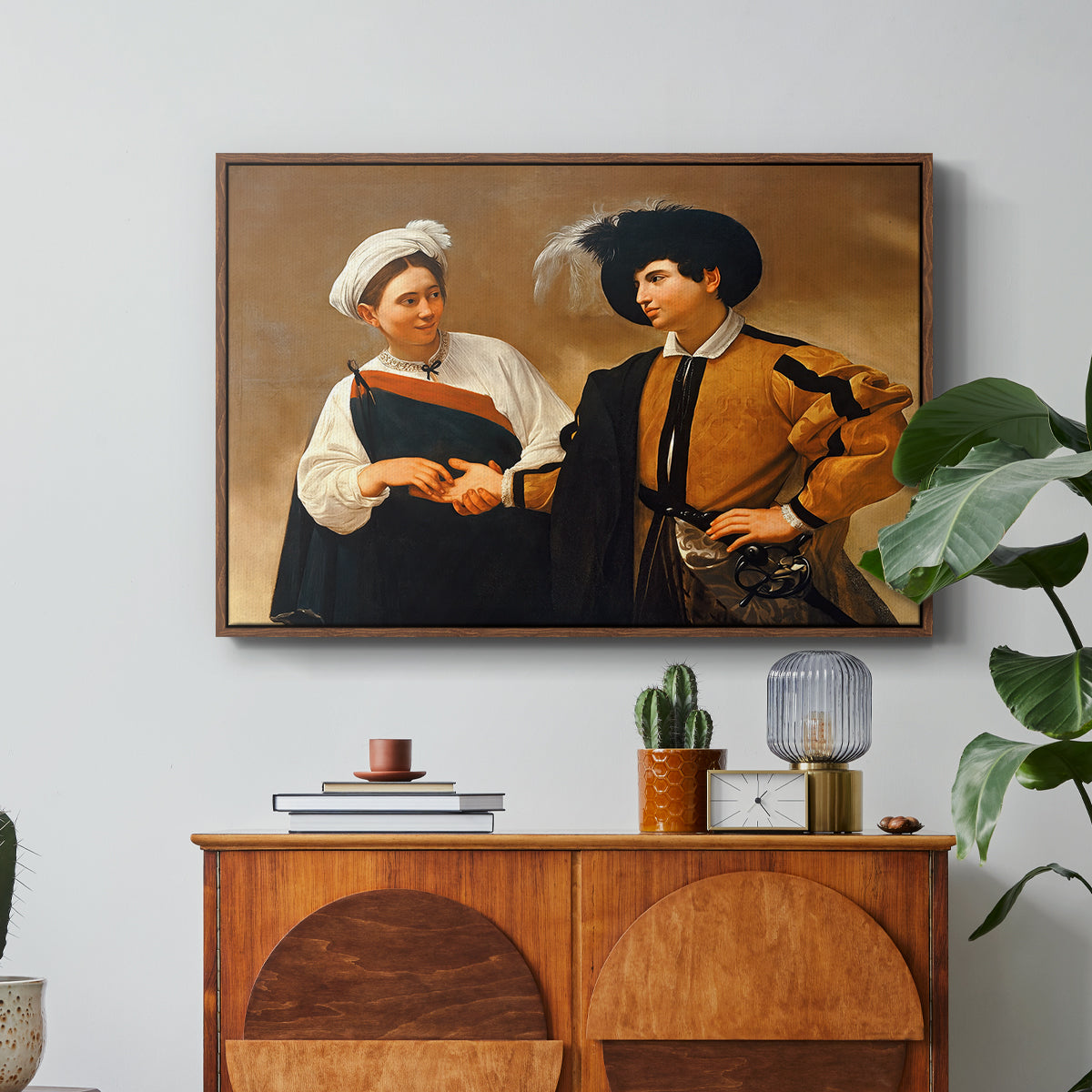 The Fortune Teller (Capitoline Version), c. 1599 by Caravaggio in a walnut floater framed canvas featuring a woman reading man's palm while discreetly removing his ring, displayed above a wood console cabinet.