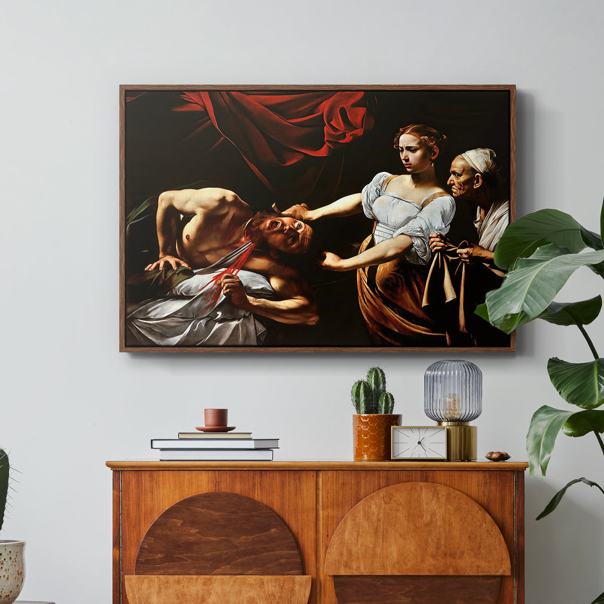 Judith Beheading Holofernes, c. 1599 by Caravaggio in a walnut floater framed canvas featuring Judith cutting off Holofernes' head as maidservant assists beside her, displayed above a wood console cabinet.