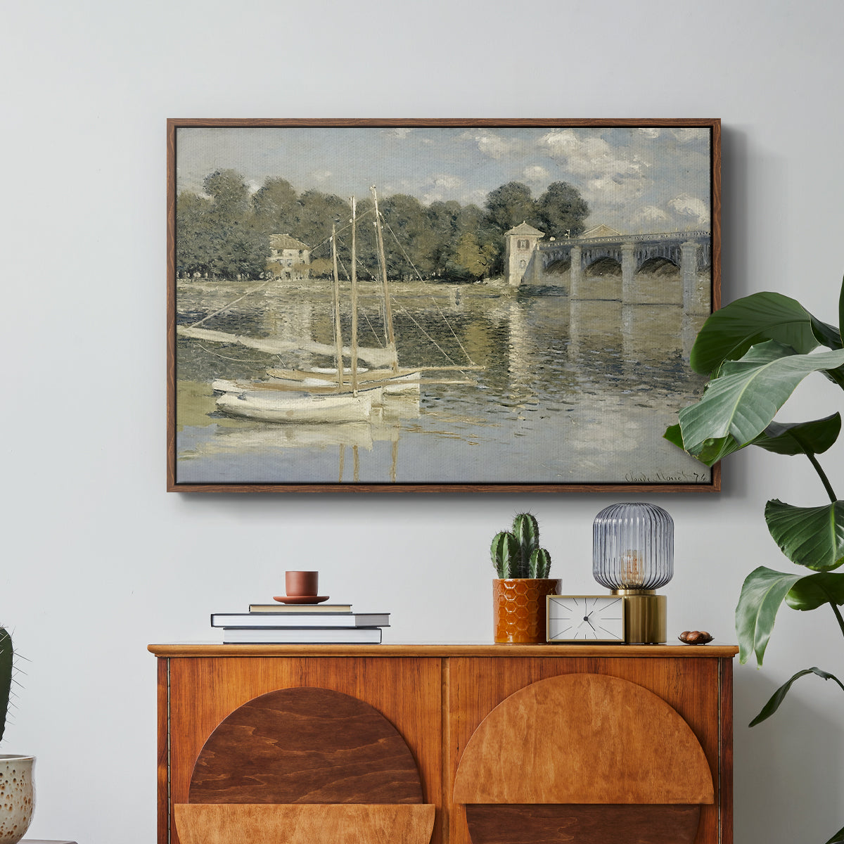 The Bridge at Argenteuil, 1874 by Claude Monet in a walnut floater framed canvas featuring a bridge spanning river with sailboats and reflections in water, displayed above a wood console cabinet.