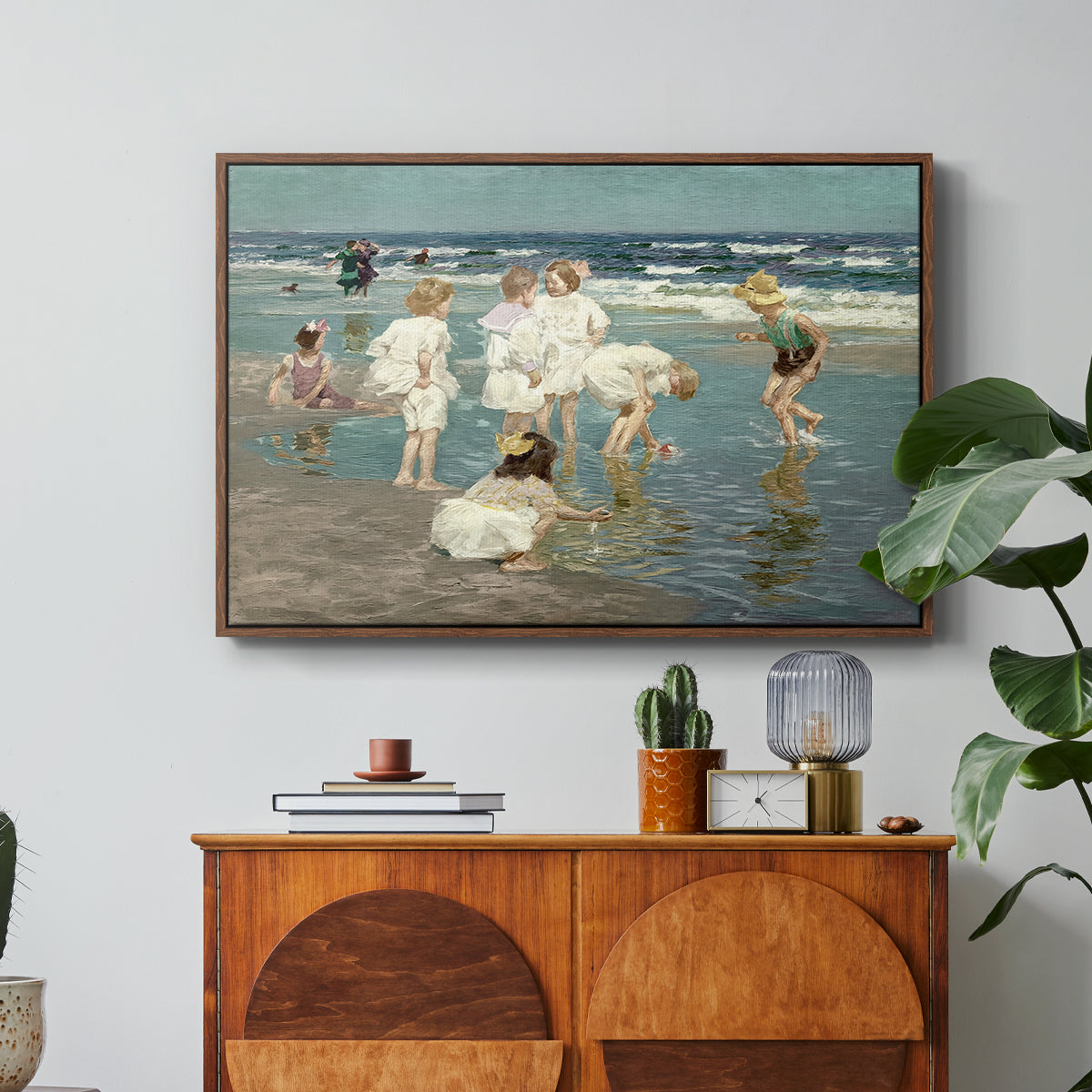 A Holiday, c. 1915 by Edward Henry Potthast in a walnut floater framed canvas featuring people relaxing and wading in shallow ocean water along a sunny beach, displayed above a wood console cabinet.