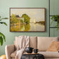 Walnut floater framed canvas featuring a peaceful village scene with houses bordering water, displayed above a sofa in a modern living room.