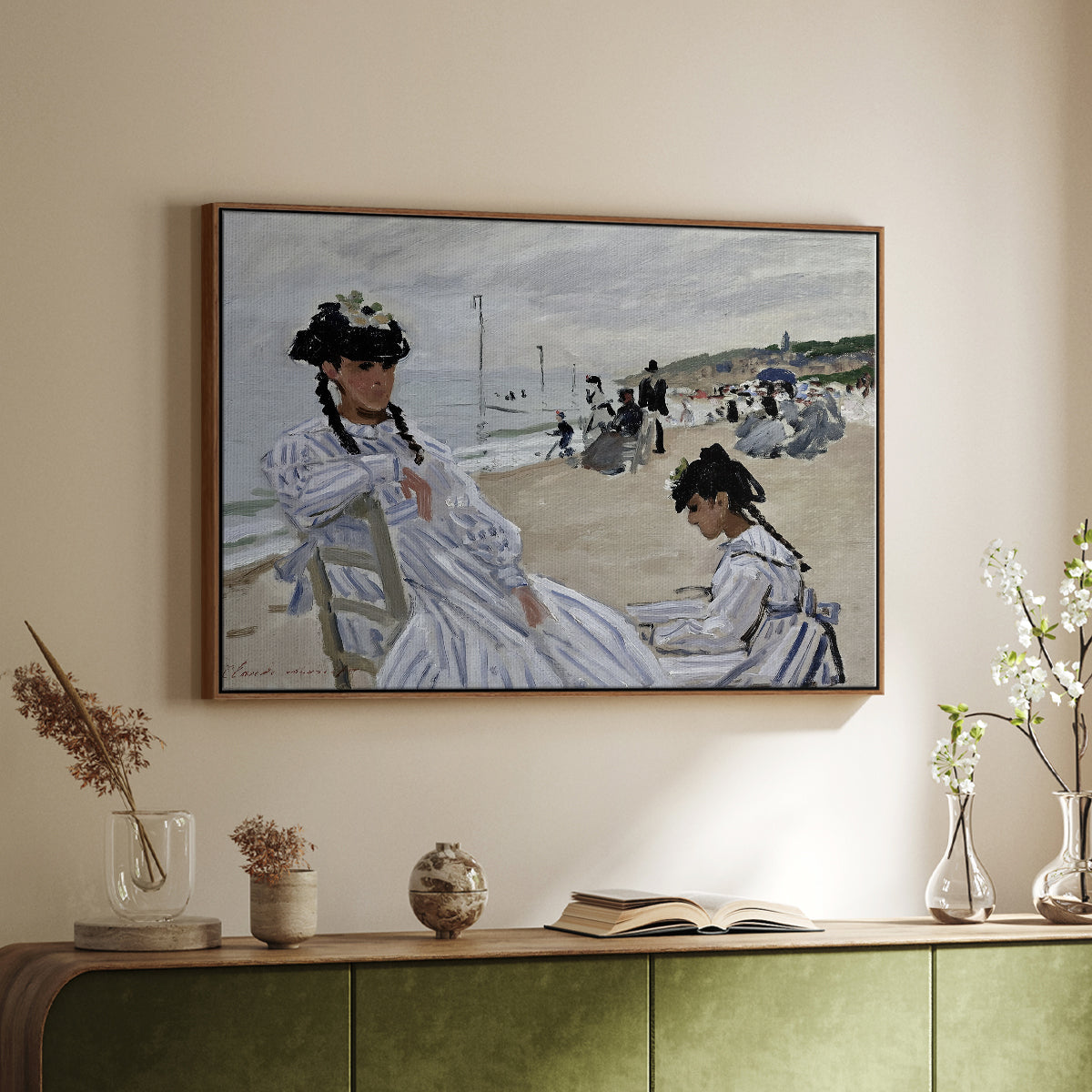 Walnut floater framed canvas of On the Beach at Trouville, 1870 by Claude Monet, featuring an impressionist seaside scene with women in dresses and hats above a sideboard in a softly lit hallway.