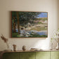 Walnut floater framed canvas of On the Bank of the Seine, Bennecourt, 1868 by Claude Monet, featuring a peaceful riverside scene with figures resting in grassy area by water above a sideboard in a softly lit hallway.
