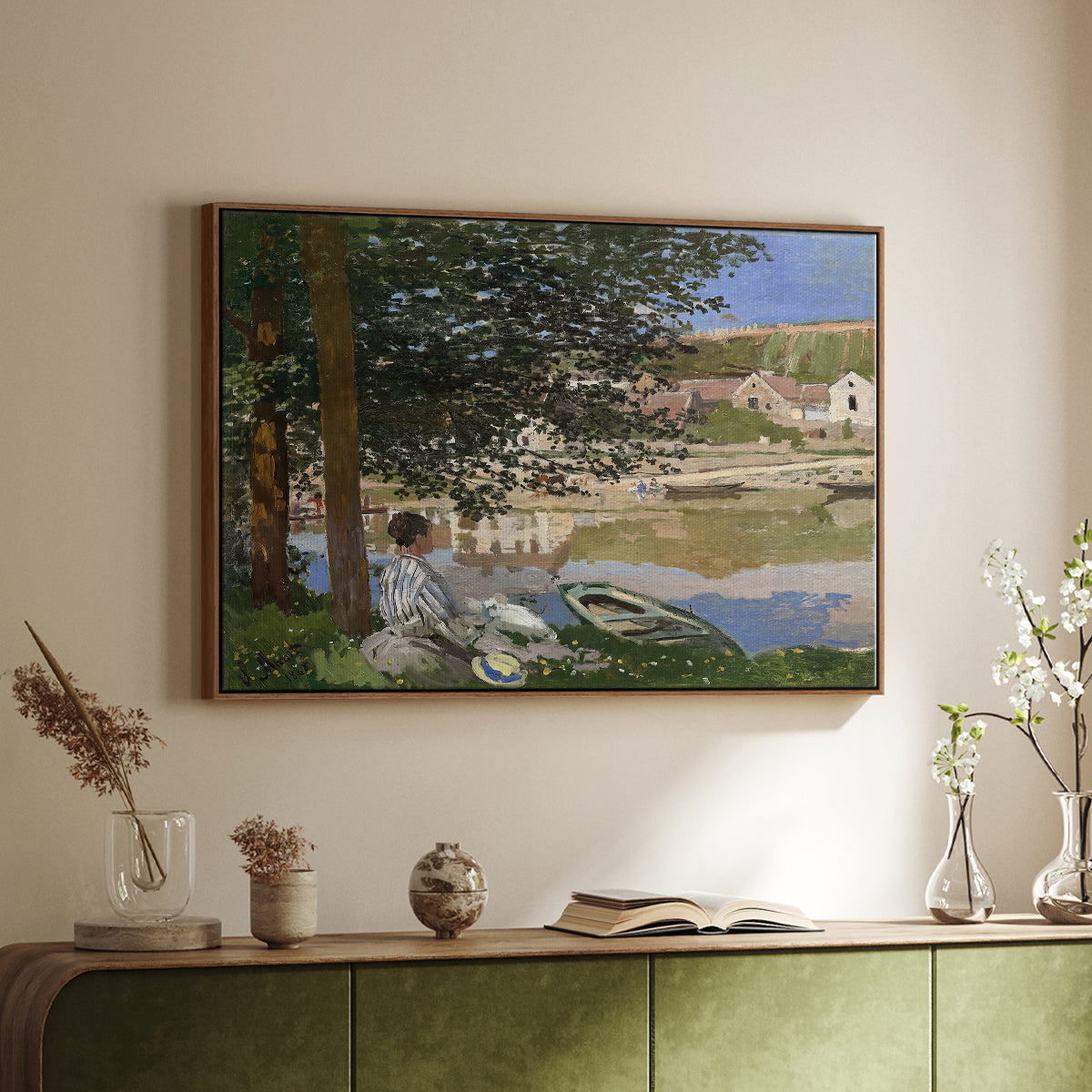 Walnut floater framed canvas of On the Bank of the Seine, Bennecourt, 1868 by Claude Monet, featuring a peaceful riverside scene with figures resting in grassy area by water above a sideboard in a softly lit hallway.