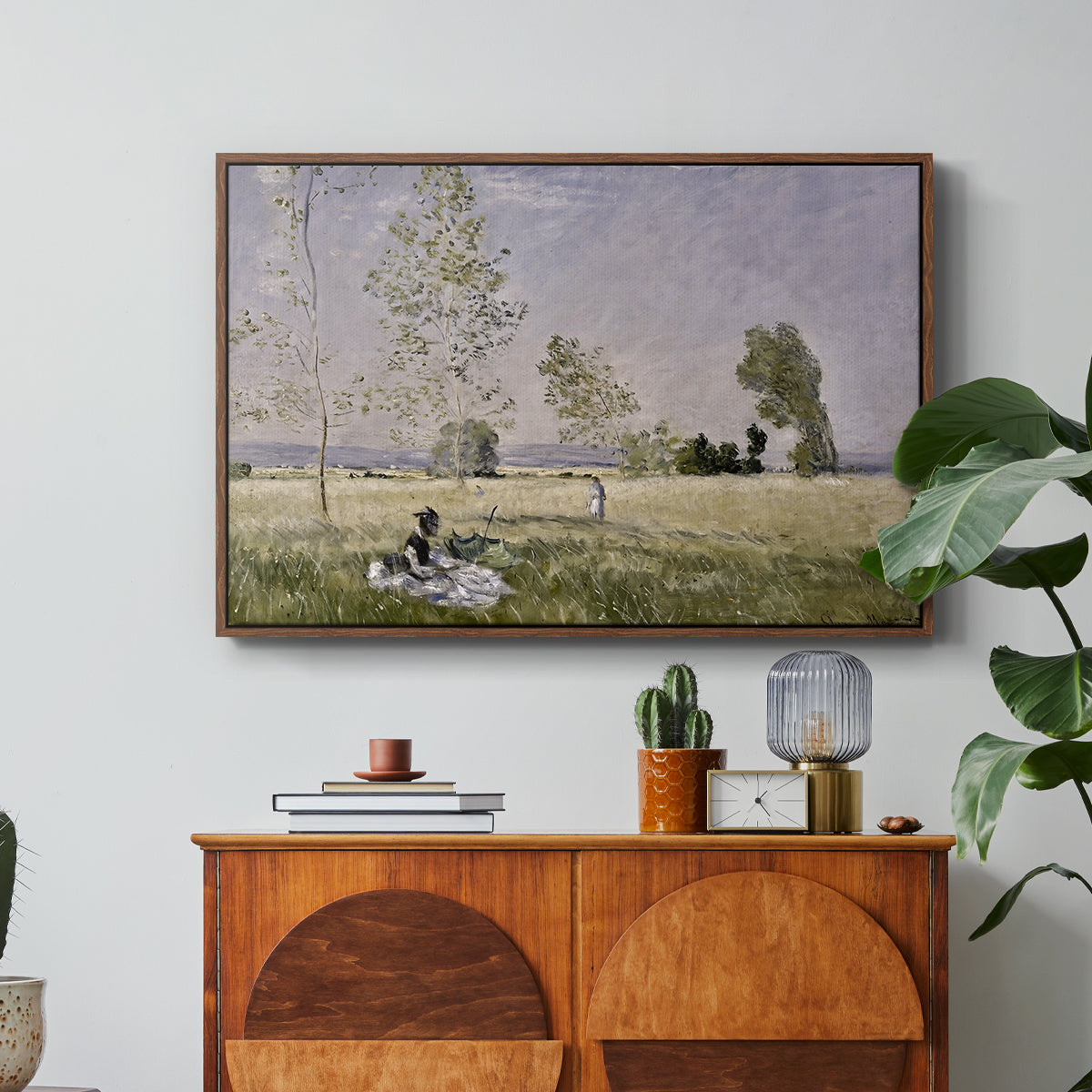 Summer (L'ete), 1874 by Claude Monet in a walnut floater framed canvas featuring a woman seated in grassy field beneath tree in bright summer landscape, displayed above a wood console cabinet.