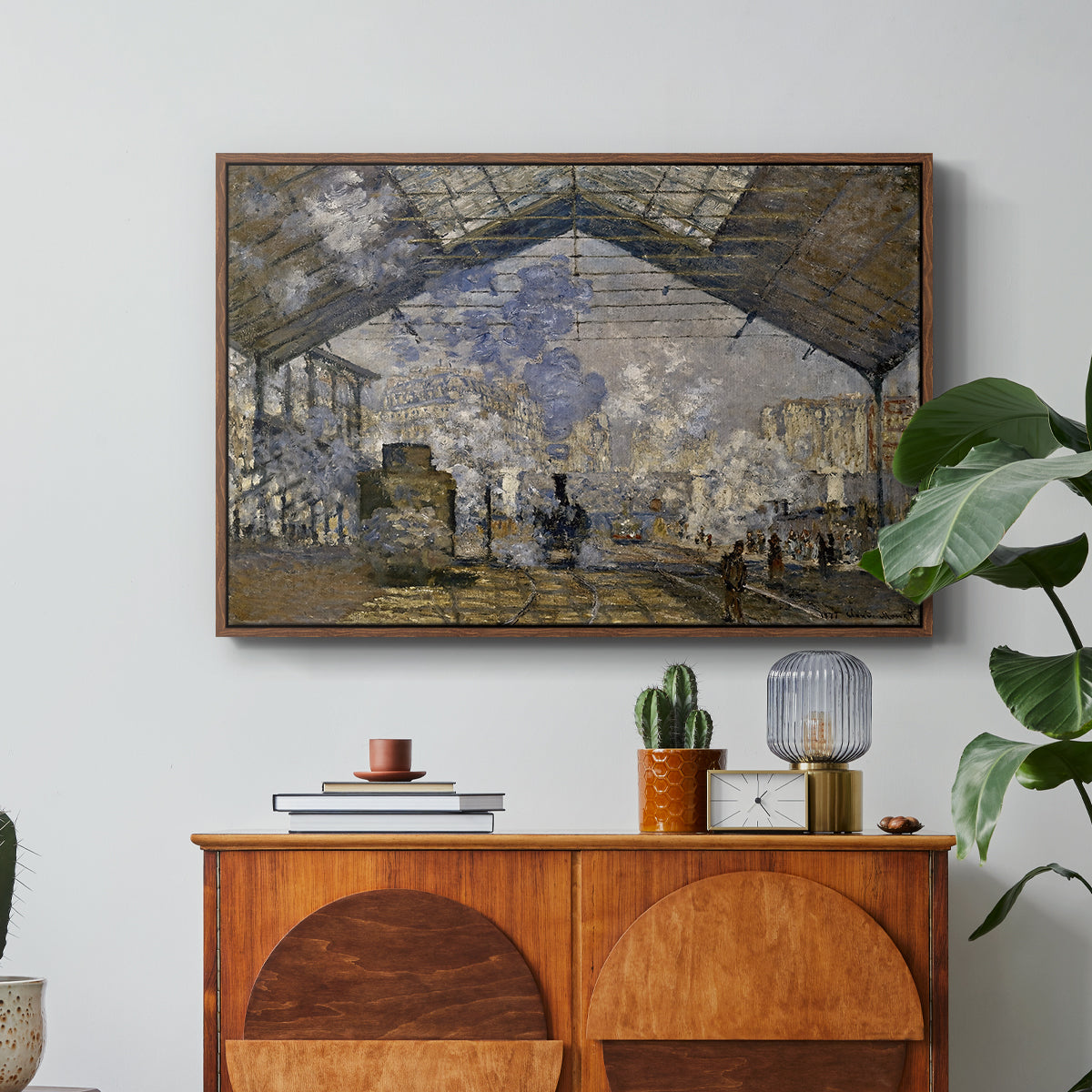 The Gare Saint-Lazare, 1877 by Claude Monet in a walnut floater framed canvas featuring a train station interior filled with steam and locomotives under iron structure, displayed above a wood console cabinet.