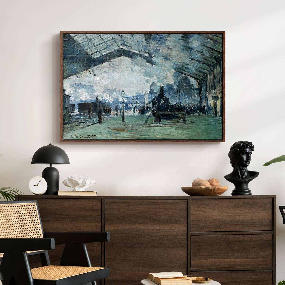 The Saint-Lazare Station, 1877 by Claude Monet displayed in a walnut floater framed canvas above a dark wood credenza in an entryway.