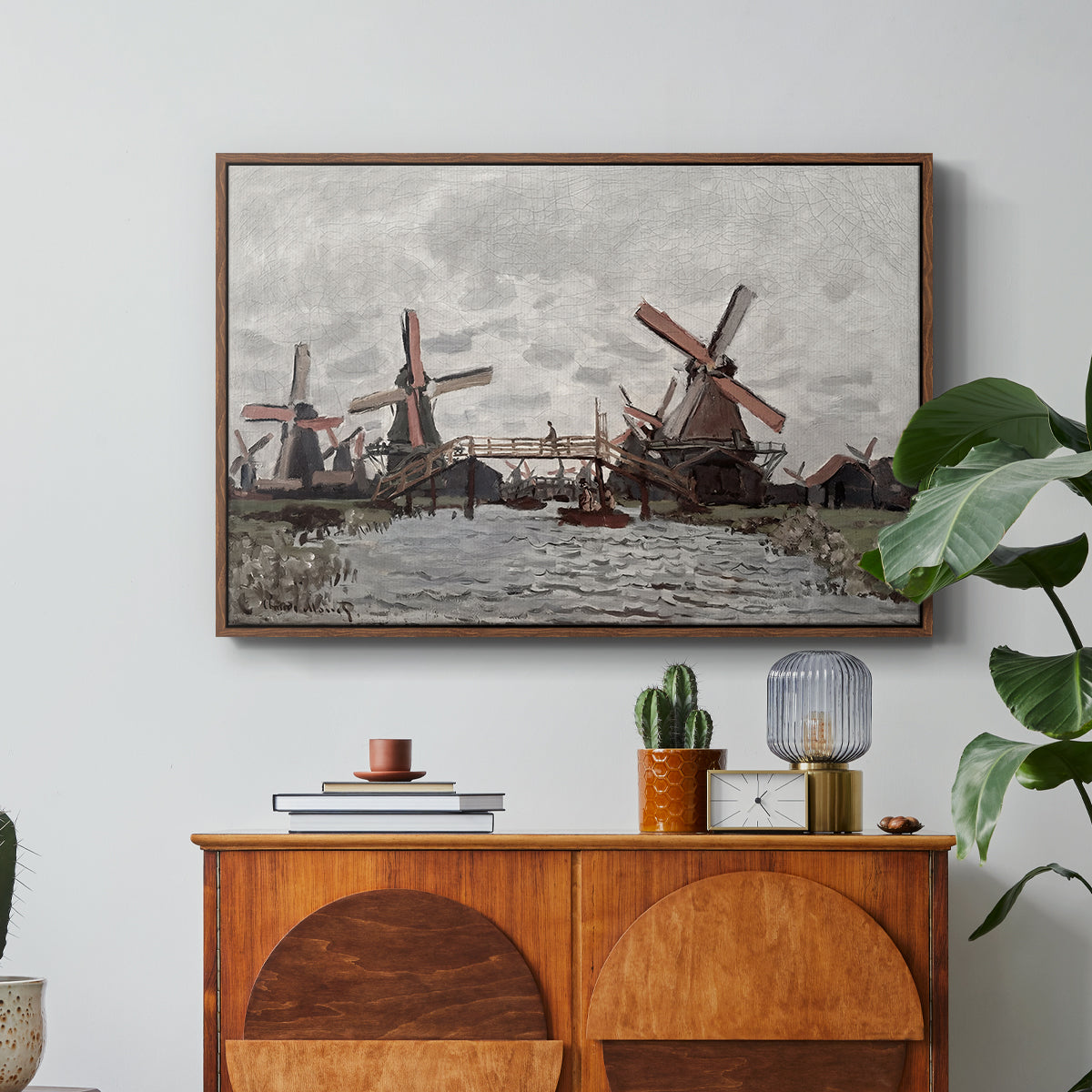 Windmills near Zaandam, 1871 by Claude Monet in a walnut floater framed canvas featuring windmills standing beside water under open sky in rural landscape, displayed above a wood console cabinet.