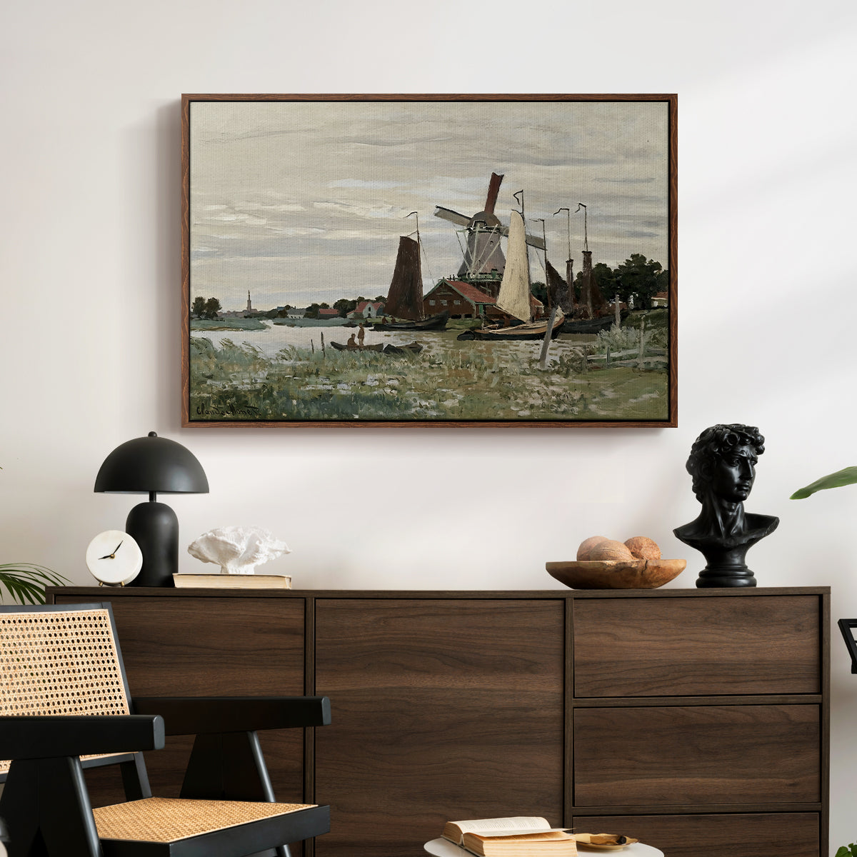 Windmill at Zaandam, 1871 by Claude Monet displayed in a walnut floater framed canvas above a dark wood credenza in an entryway.
