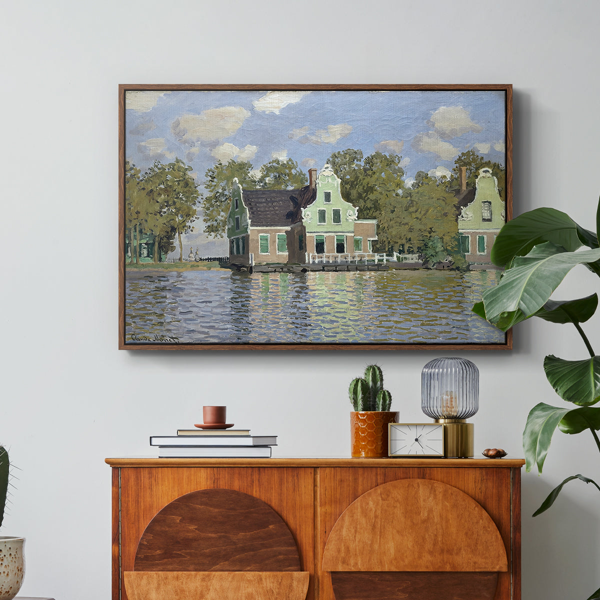 Houses on the Zaan River at Zaandam, 1871 by Claude Monet in a walnut floater framed canvas featuring a row of houses along river with reflections in calm water, displayed above a wood console cabinet.